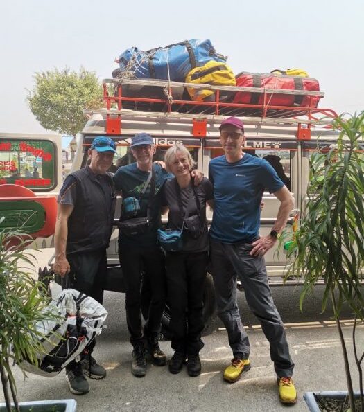 The clibmers stand in a town, in front of a truck carrying their duffel bags on the roof.