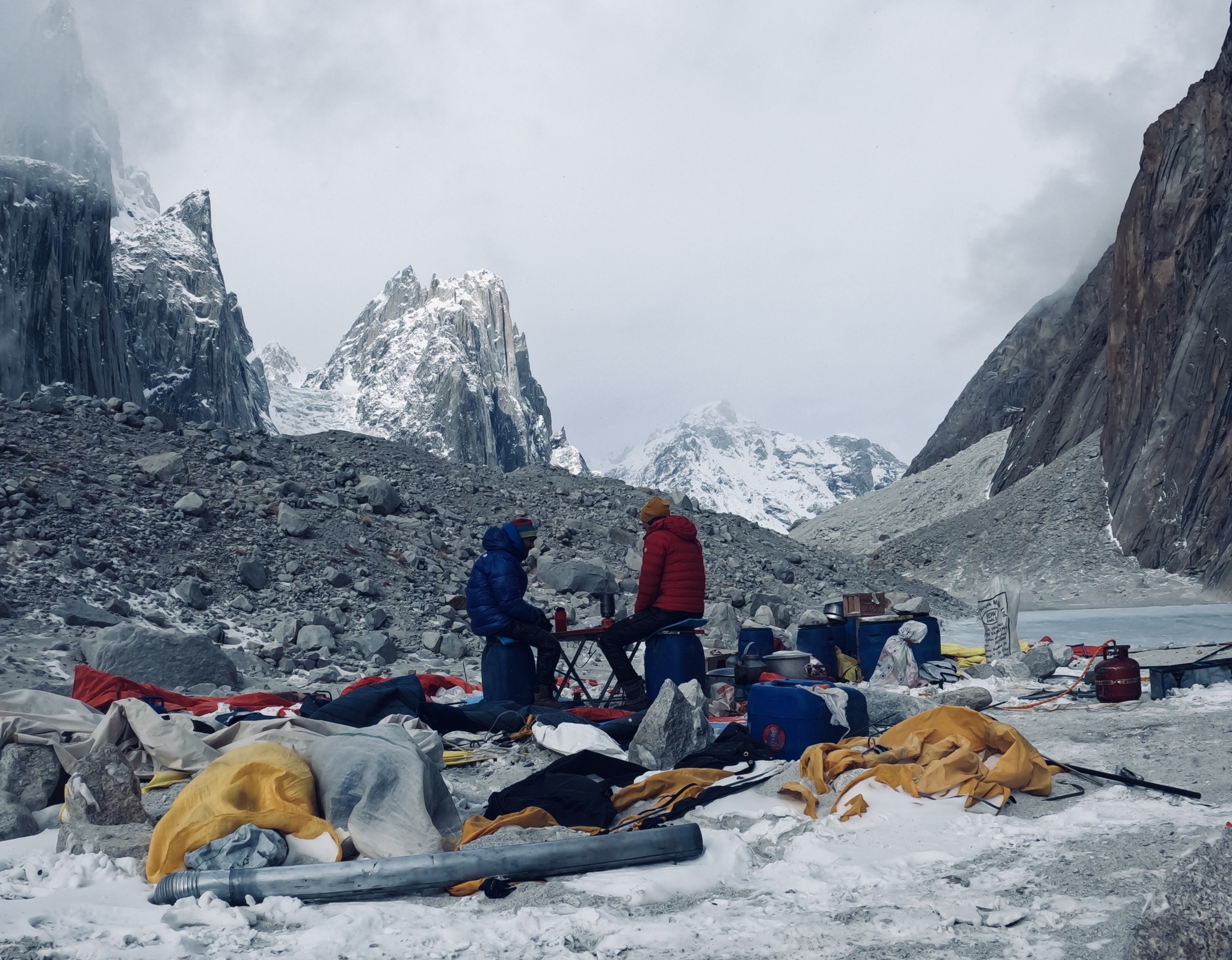 Climbers sitting on two chairs, surrunded by rags of tent and scattered items.