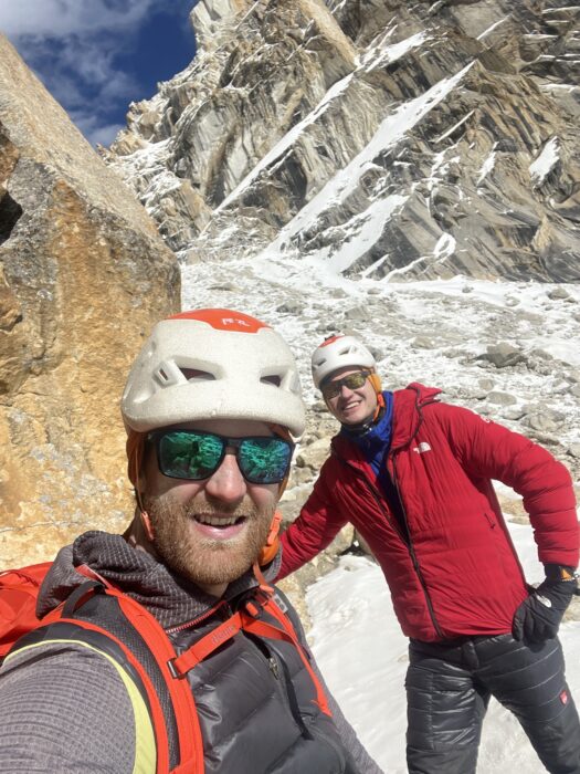 The climbers with helmets and sun glasses in front of a glaicer and with peaks in background.