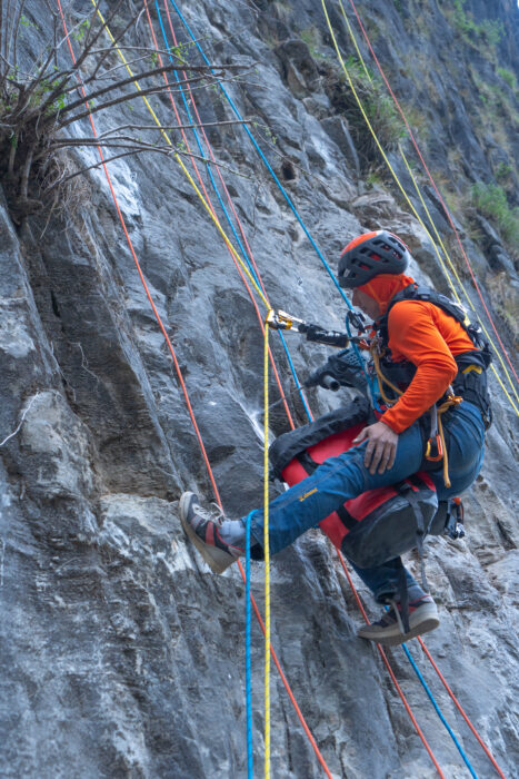 Malla secured with ropes at a wall, a Hilti drill in his hand. 