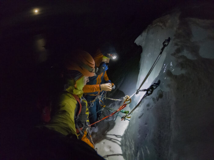 the climbers at an ice belay in pitch black darkness, the moon in background.