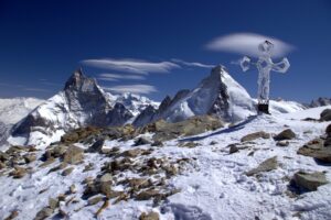 A snowy summit with a cross marking it, and high peaks in background.