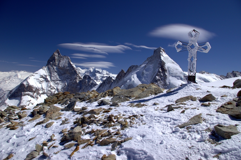 A snowy summit with a cross marking it, and high peaks in background.