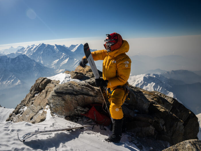 Ziemski, in a yellow suit, prepares to put his skis on the snow. 