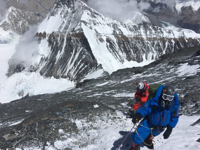 Climbers on a fixed ropes on rock and ice terrain, on top of a ridge. 