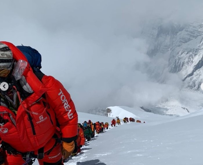 Nearly a hundred climbers in line up a snow ramp.