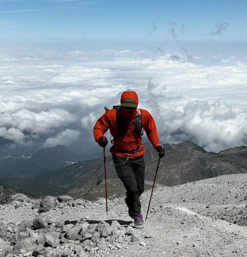fisher running on rocky mountain ground, clouds behind him.