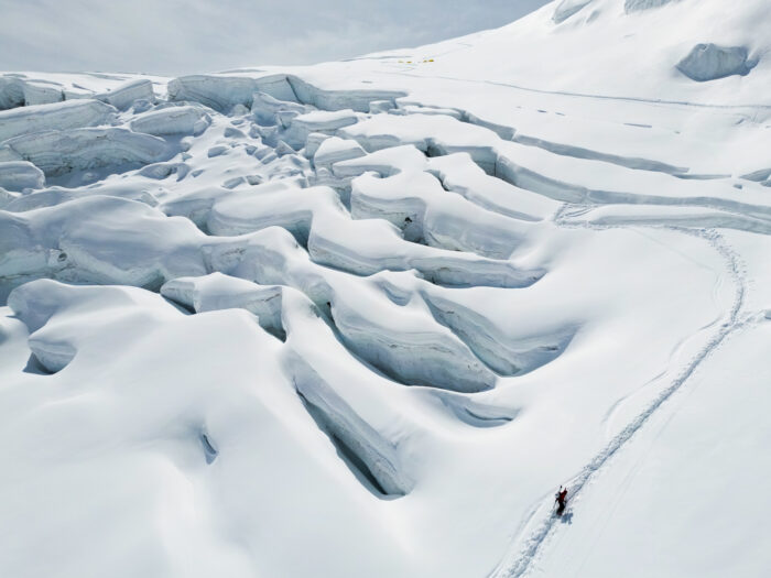 a skier climbing with skins on the right side of a serac barrier. 