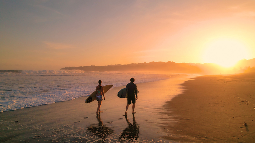 silhoeutte of two surfers at sunst on beach