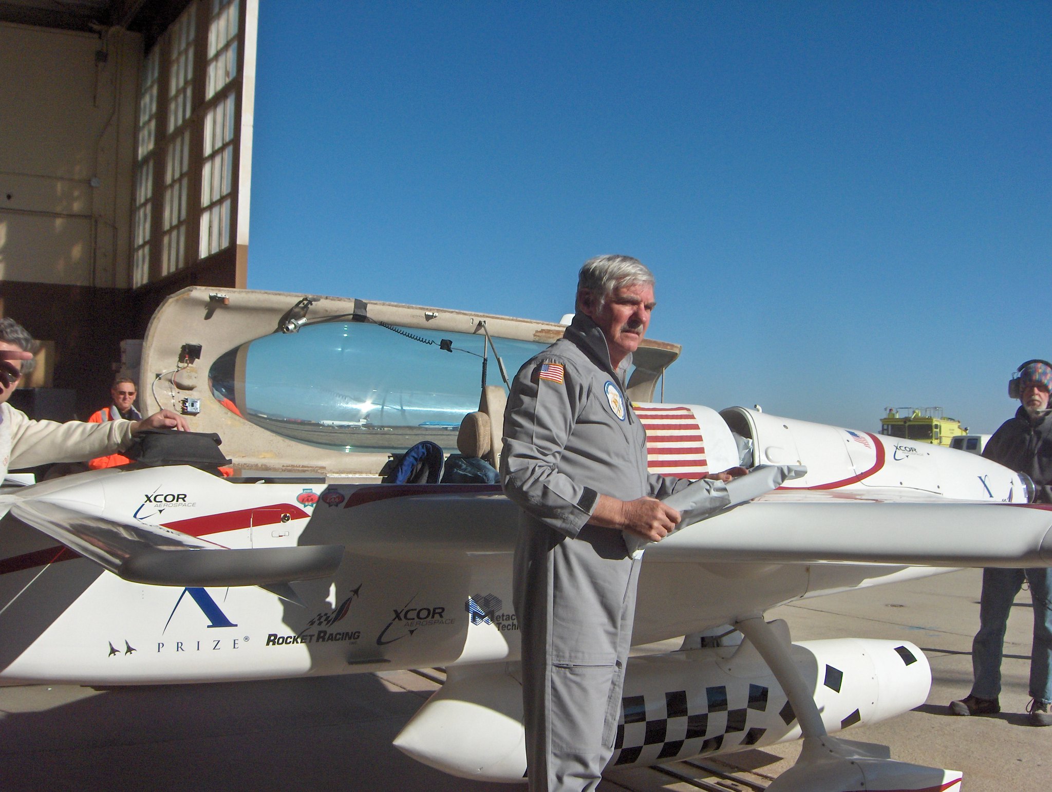 gray-haired pilot in flight suit with aircraft