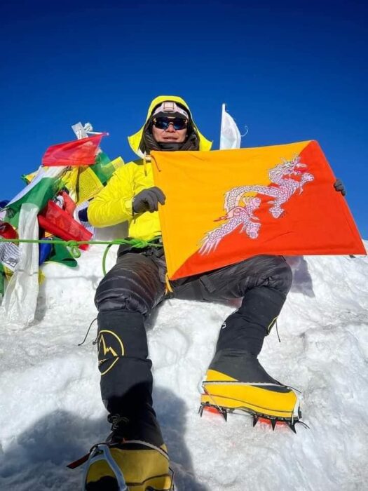 Jigme Pelden Dorje holds the flag of Bhutan while sitting on Everest summit.