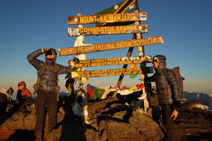 The couple poses at sunrising by the board on Kiliamanjaro summit
