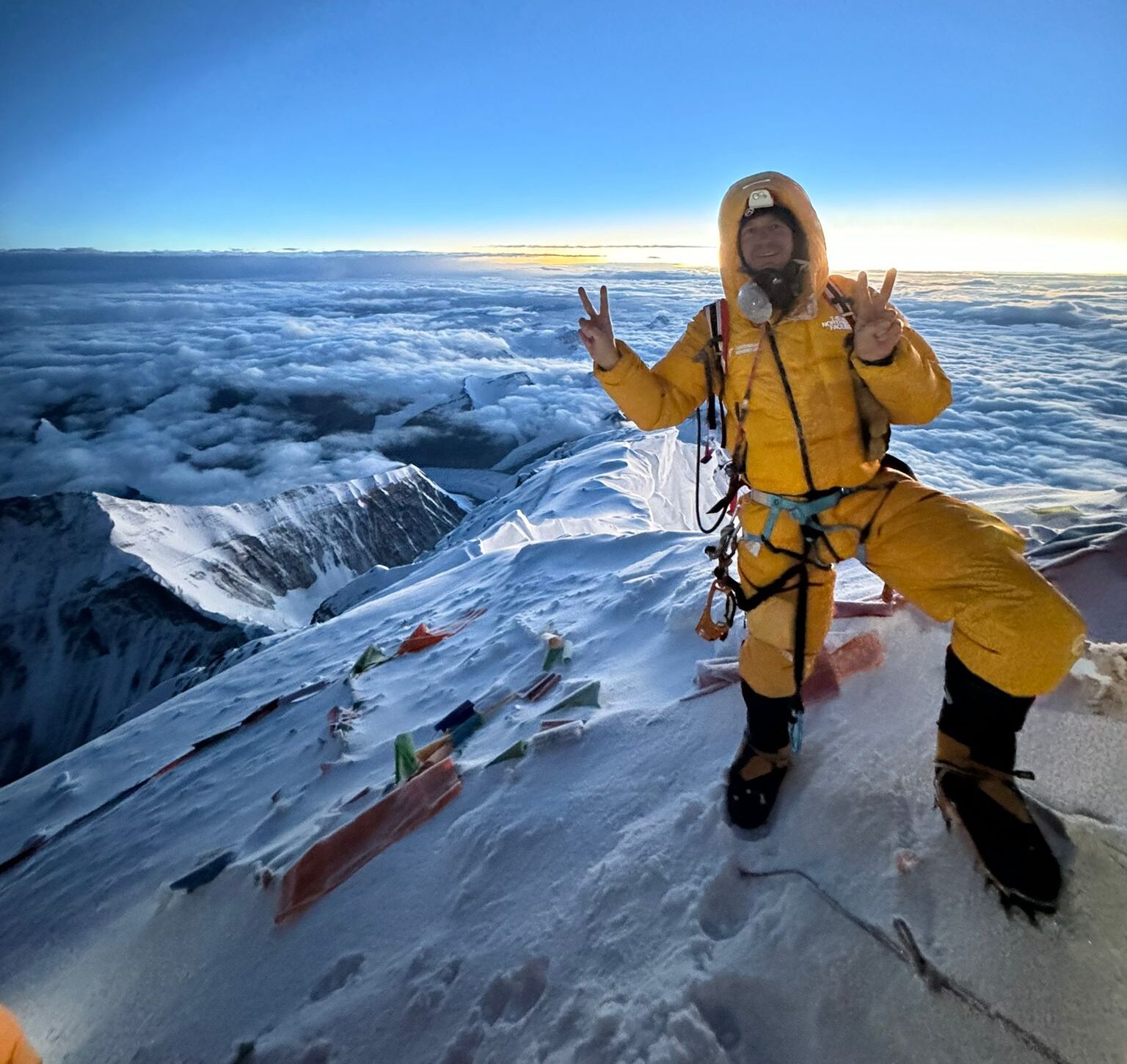 a climber points four fingers on the summit of Everest