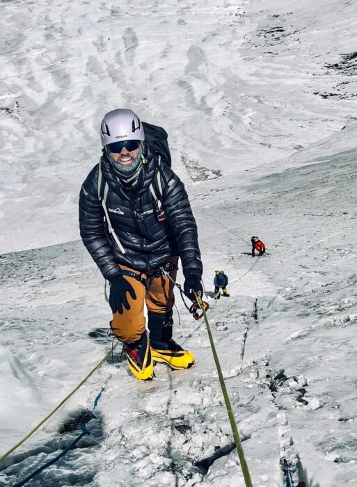 the climber is clipped to a fixed rope and stands on crusty, icy ground.