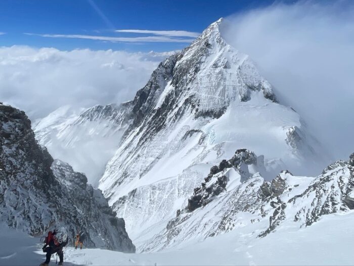 The clibmers prgress on Lhotse with Everest wrapped in clouds behind.