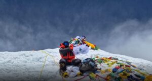 The climber on the summit, holding a flag in sunny but very windy weather