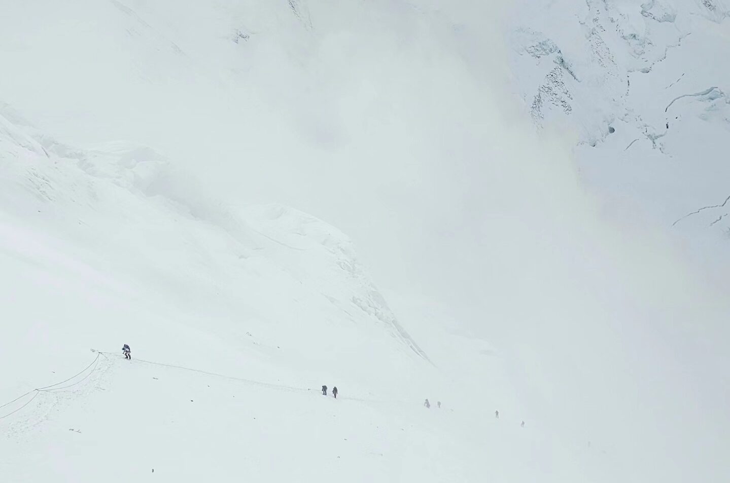 tiny figures of climbers on a huge, while slope on a foggy day on Everest as they climb the Lhotse Face
