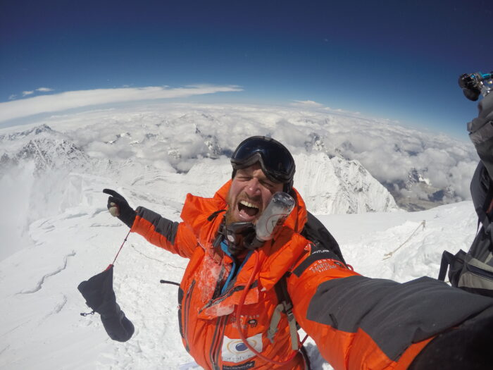 Veyt screams to the camera in triumph from the summit of Everest, mountains around and below him.
