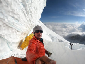 sajid takes a selfie under a serac, with a sea of clouds behind him.