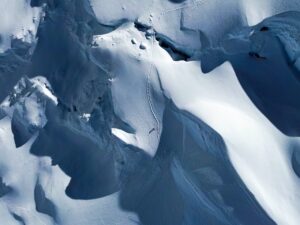 A climber by a line of footprints among snow-covered seracs.