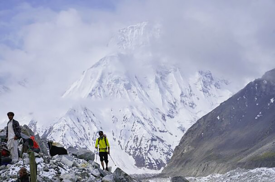 Climbers on a trail with a formidable mountain face behind them.