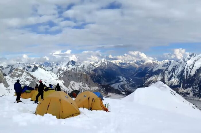 Climbers by a small group of tents on a snowy col on Spantik