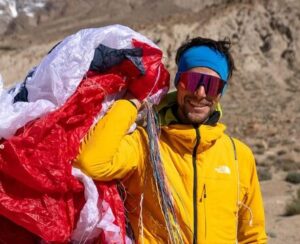 Vedrines smiles while holding his paraglide over one shoulder.