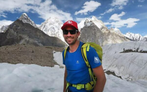 The climber in a t-shirt with jagged peaks in background.