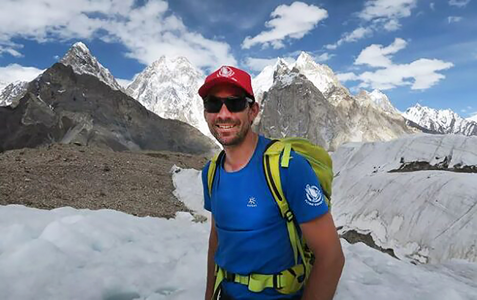 The climber in a t-shirt with jagged peaks in background.