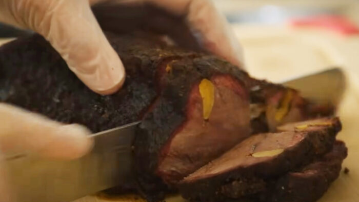 a hand slices a thick chunk of meat