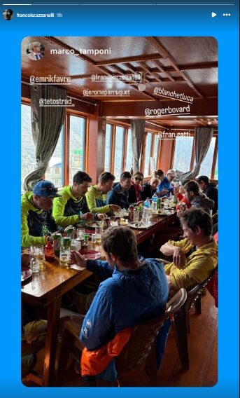 The climbers sitting at a long table in a lodge with windows all around.