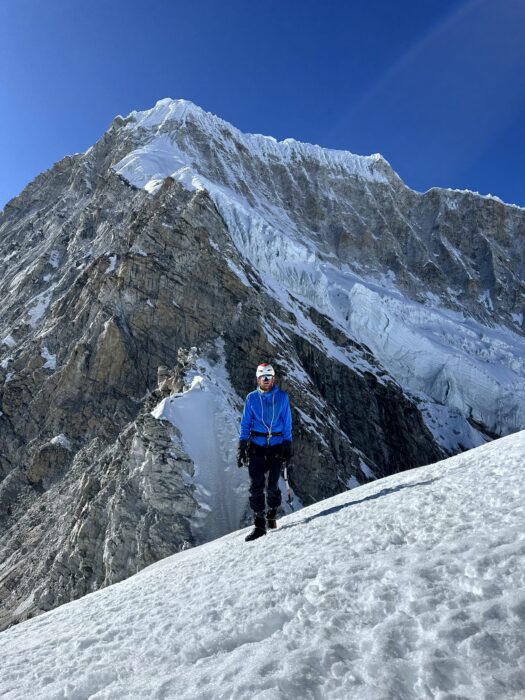 a climber on a snow slope with a peak behind him.
