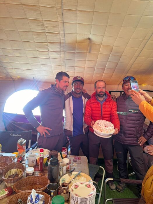 Climbers smail and hold a summit celebration cake in a mess tent.