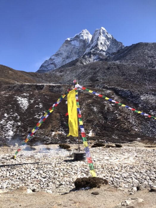 A pole with prayer flags on a flattened rocky surface in a mountain area.