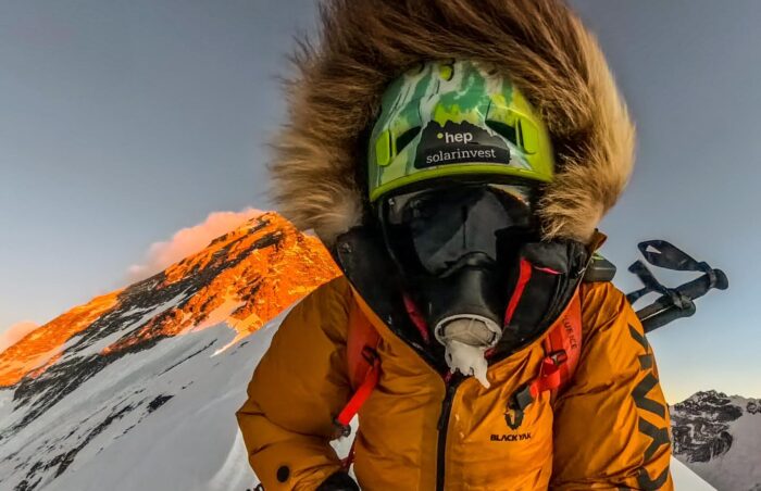 Jost Kobusch in full winter, high-altitude attire, with the summit of Everest behind him.