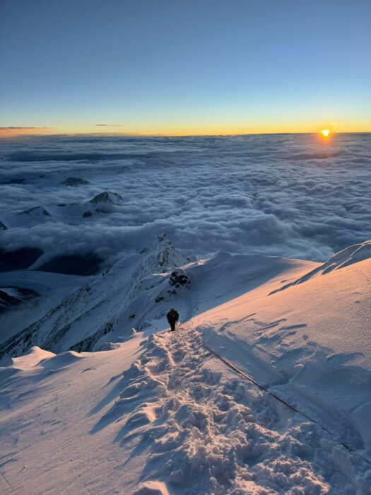 A climber on a snow slope with tracks from previous climbers and a rope.