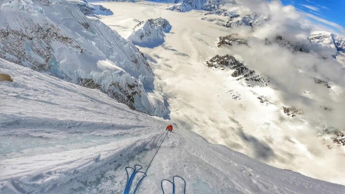 a climber at the end of a rope on an endless, vertical ramp of ice, as seen from above. 