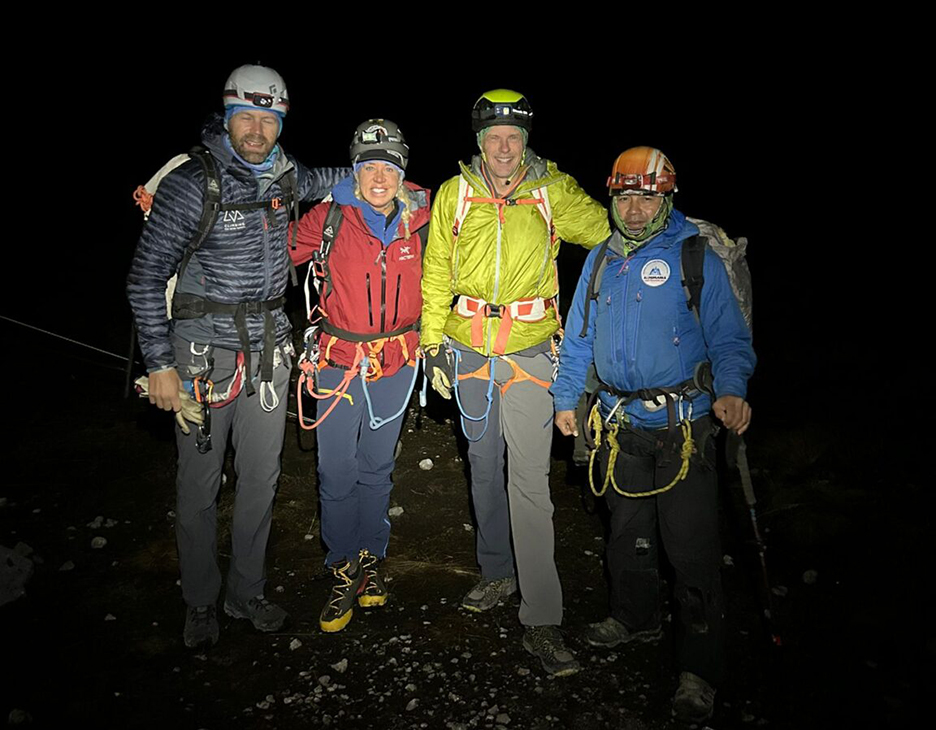 a group of climbers with harnesses and helmest pose in the dark
