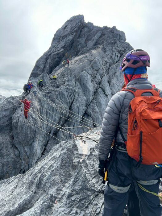 A guide checks a client while they cross a tyrolean traverse on Castensz Pyramid.