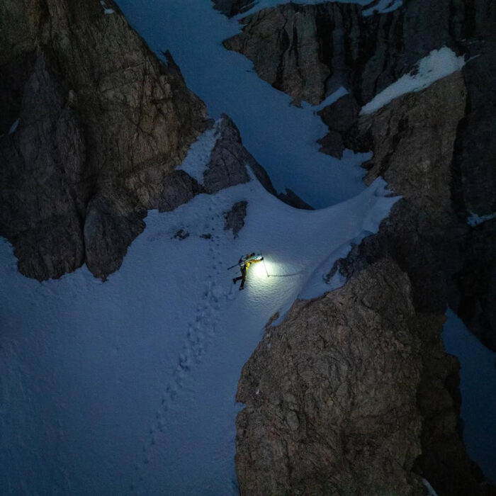 A climber skis down a snow gully in the dark.
