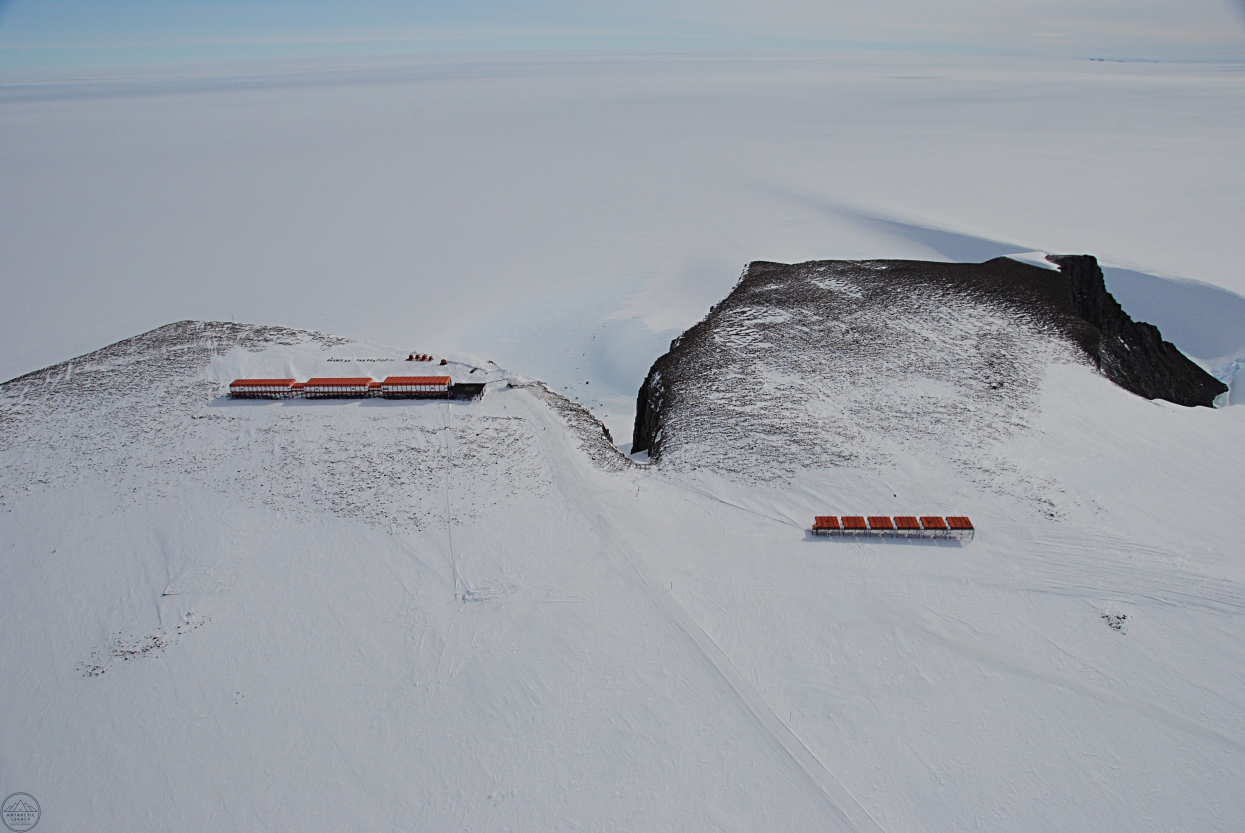 An aerial shot of the SANAE IV base, a series of red buildings in a vast Antarctic landscape.