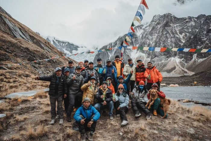 A group of climbers cheer in front of a chrten with prayer flags at Annapurna Base Camp.