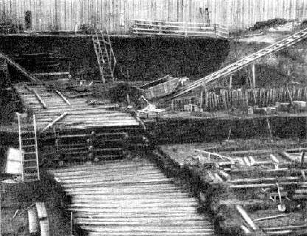 Grainy black and white photo of an old wooden boardwalk half-buried in earth.