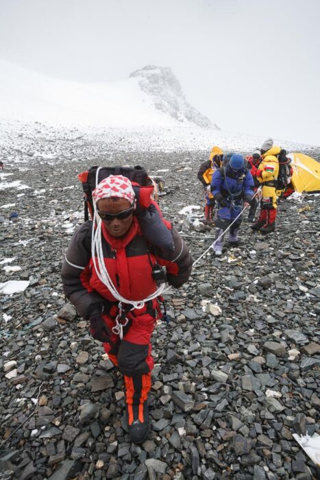 A sherpa leads a rope with a sick climber tied to the other side, on the rocky ground of the south col of Everest.