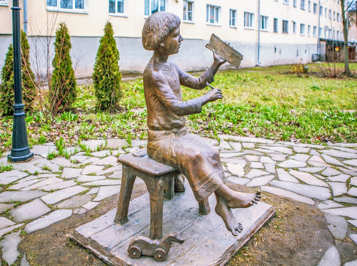 A bronze statue of a young boy sitting on a bench, writing.