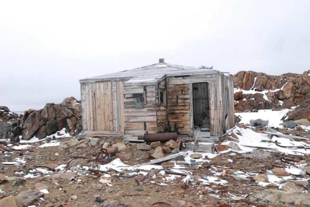 A small wooden cabin on an icy, muddy ground.