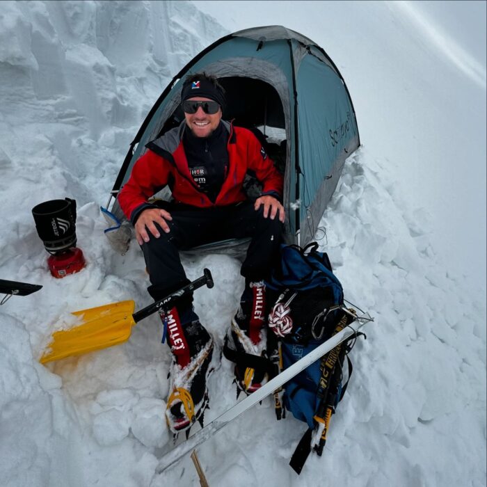 Vadim Druelle sitting in front of a tiny tent pitched in the snow.