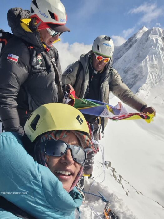 A sherpa witth two clients unfolds a roll of flags on a snowy summit.