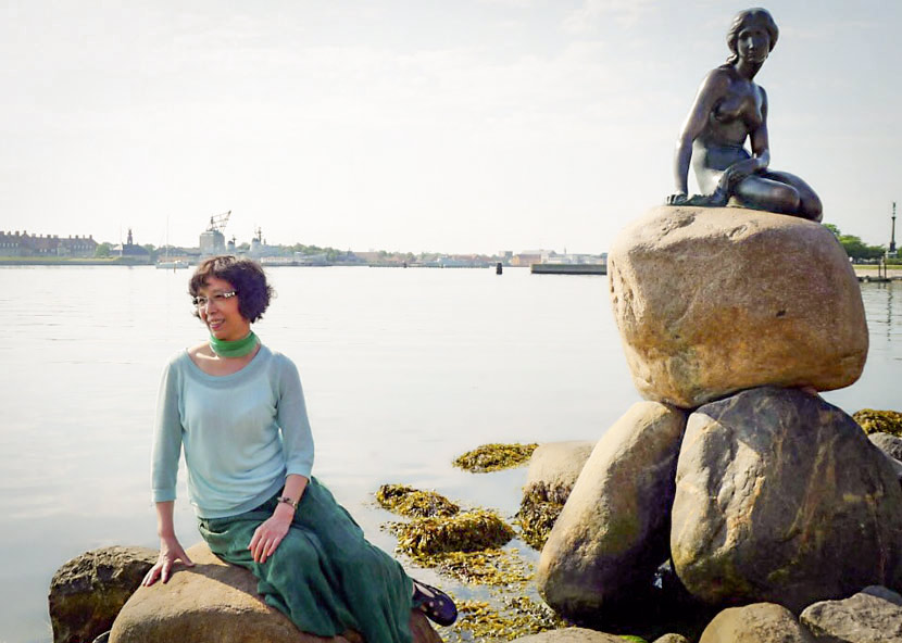 A woman posing next to a statue of a mermaid.