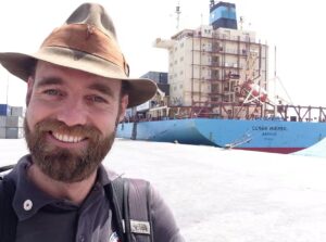 bearded man smiling in front of ship